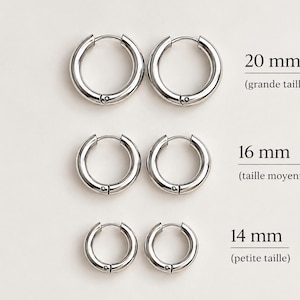 Peut inclure: Trois paires de créoles argentées disposées en rangées. La paire du haut est étiquetée 20 mm, la paire du milieu 16 mm et la paire du bas 14 mm. Chaque anneau présente une finition lisse et polie avec un mécanisme de fermeture à charnière.