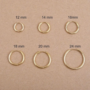 Peut inclure: Une collection de six boucles d'oreilles créoles dorées de différentes tailles, allant de 12 mm à 24 mm de diamètre. Les boucles d'oreilles sont présentées sur une surface neutre, mettant en valeur leur design circulaire simple. Les tailles sont clairement indiquées.