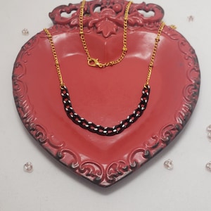 Könnte beinhalten: Eine schwarz-weiße Kettenkette mit goldenen Akzenten auf einer roten herzförmigen Schale. Die Kette besteht aus kleinen, miteinander verbundenen Quadraten mit einem weißen Rand und einer schwarzen Mitte.