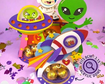 May include: Digital SVG file for Cricut and Silhouette featuring paper craft space-themed treat holders. Includes a purple UFO, a white rocket, a green alien, and an astronaut. The designs feature clear 8cm or 3.15 inch acrylic domes for treats.