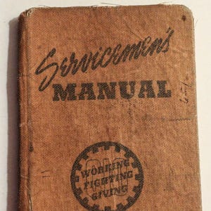 May include: A brown, worn, canvas-covered book with the title "Servicemen's Manual" printed in black. The book has a black and white circular stamp with the words "Working, Fighting, Giving" inside.