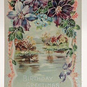 May include: Vintage birthday greeting card featuring a watercolor landscape with a lake, trees, and houses. The card is framed by a floral border of purple and blue flowers. The words "BIRTHDAY GREETINGS" are printed on the card.