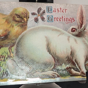 Peut inclure: Carte postale de Pâques vintage avec un poussin et un lapin dans un jardin. Le poussin est jaune et marron, et le lapin est blanc. La carte postale porte les mots "Joyeuses Pâques".