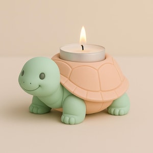 Op de afbeelding: Een teal en perzikvormige kaarsenhouder in de vorm van een schildpad met een brandende witte kaars. De schildpad heeft een lachend gezicht en een getextureerd schild. Het is een decoratief item.