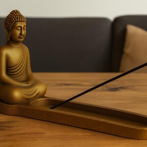 Könnte beinhalten: Eine goldfarbene Buddha-Statue mit passendem Räucherstäbchenhalter. Der Buddha befindet sich in einer sitzenden Meditationshaltung. Ein schwarzer Räucherstäbchen ist im Halter, der eine längliche ovale Form hat.