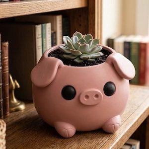 May include: A pink pig-shaped planter with a succulent plant. The planter has black eyes, a small snout, and small feet. It sits on a wooden shelf in front of a bookshelf.
