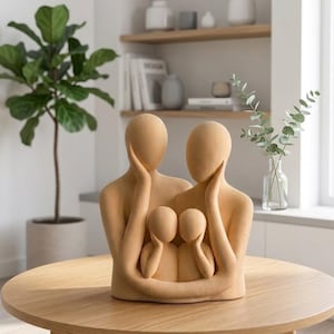 May include: A beige family sculpture depicting two adults embracing two children. The figures have smooth, featureless faces and are posed on a round wooden table. The sculpture is a decorative item for a home.