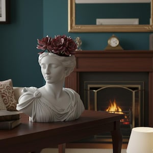 Puede incluir: Busto blanco de mujer de diseño clásico, con flores de color burdeos en la cabeza. El busto está colocado sobre una mesa marrón oscuro. El fondo incluye una chimenea, un espejo y una pared turquesa.