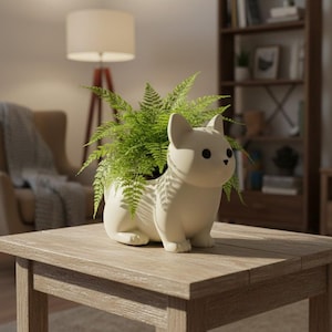 May include: A cream-colored ceramic dog planter with a fern plant inside. The dog planter is sitting on a wooden table. The dog planter has black eyes and a cute, friendly expression. The fern plant has bright green leaves.