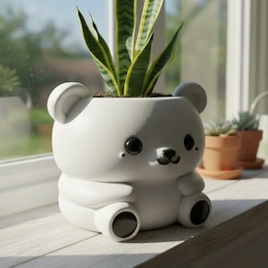 May include: A white, bear-shaped planter with a smiling face, holding a green and yellow plant. The planter has black eyes and a black nose. The planter is sitting on a windowsill.