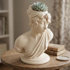 May include: A cream-colored bust planter in the style of classical sculpture, with a succulent plant in the head. The planter has a round base and is placed on a wooden table. The succulent has pale green leaves.