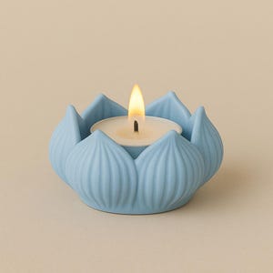 May include: A light blue ceramic lotus flower-shaped candle holder with a lit tea light candle. The candle holder has detailed petal designs and sits on a neutral background. The flame is bright yellow.