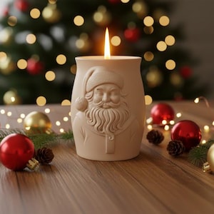 May include: A lit candle in a beige Santa Claus-themed holder sits on a wooden surface, surrounded by red and gold Christmas baubles, pine sprigs, and fairy lights. A Christmas tree with blurred lights is in the background.