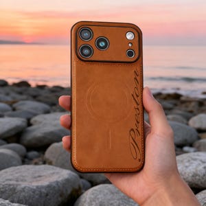 May include: A brown leather phone case with a black border. The case has a camera cutout and the name "Preston" in cursive script. A circular design is visible on the back, with a magnetic charging symbol.