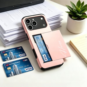 Könnte beinhalten: Eine hellrosa Smartphone-Hülle mit einem integrierten, verschiebbaren Kartenfach auf der Rückseite. Die Hülle hat einen schwarzen Kamerarahmen und eine Schiebeabdeckung mit dem Wort Honey in weißer Schreibschrift. Zwei blaue Visa-Karten liegen daneben.