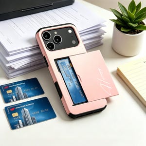May include: A light pink smartphone case with a built-in card holder slot containing a blue credit card. The case features a black camera module cutout and a script logo on the sliding cover. Two additional blue credit cards lie nearby.