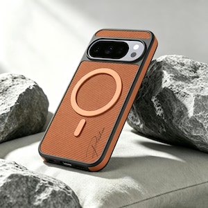 Op de afbeelding: Een smartphonehoesje met een getextureerd oranje achterpaneel en een zwart frame. Het hoesje is voorzien van een cirkelvormige magnetische oplaadring in het midden, een verticale uitlijningsmagneet en de cursieve tekst Preston rechtsonder.