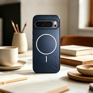 Pode incluir: Capa de telefone azul marinho com um design circular branco e o nome "Harvey" em escrita cursiva. A capa tem um recorte para a câmera e uma borda preta. A capa está em uma superfície branca.