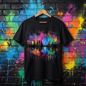 May include: Black t-shirt with a colourful graphic depicting a forest scene reflected in water, with pink, blue, and yellow hues. The design has a watercolour effect with dripping paint details. The shirt is hanging on a wooden hanger.
