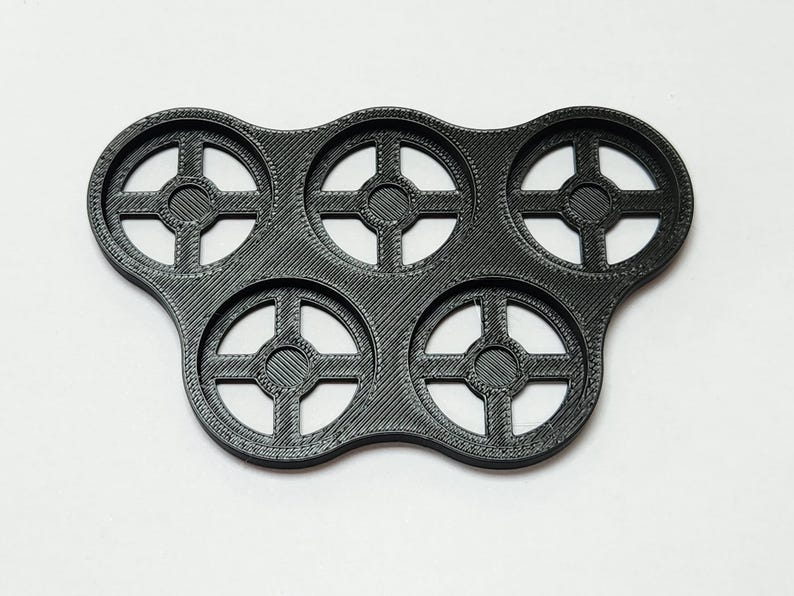 May include: A black plastic tray with six circular cutouts, each with a cross-shaped design. The tray is designed to hold small round objects.
