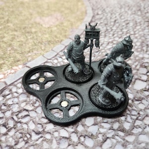 May include: A black plastic base with four circular slots for miniature figures. Each slot has a magnetic center and a raised rim. Three miniature figures are displayed on the base, two in armor and one with a banner.