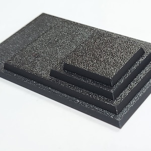 May include: Four black square-shaped platforms stacked on top of each other. The platforms are made of a textured material.