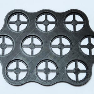May include: A black, flexible, silicone mold with 12 circular cutouts. Each cutout has a cross-shaped design.