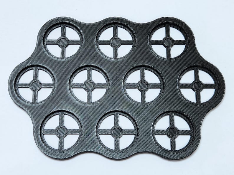 May include: A black, flexible, silicone mold with 12 circular cutouts. Each cutout has a cross-shaped design.