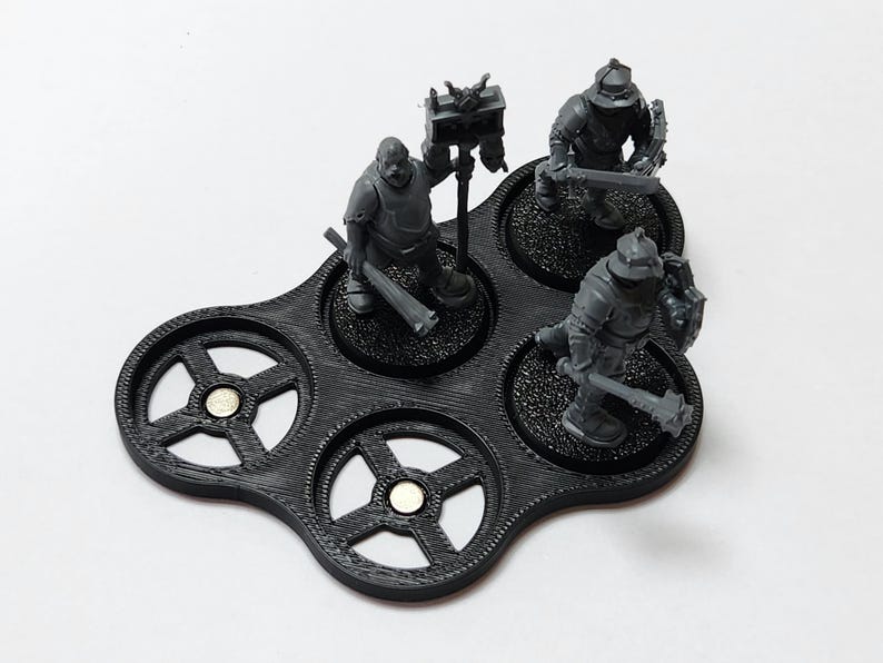 May include: A black plastic miniature figure display stand with five circular slots. Three miniature figures are displayed on the stand. The figures are gray and are holding weapons.