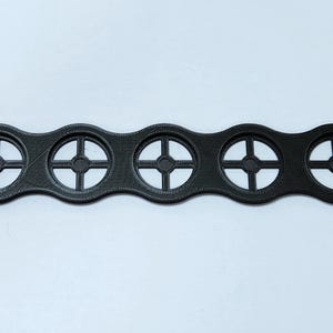 May include: A black plastic 3D printed object with five circular cutouts. Each cutout has a cross-shaped design.