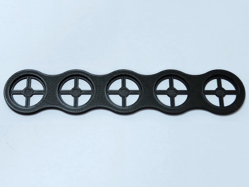 May include: A black plastic 3D printed object with five circular cutouts. Each cutout has a cross-shaped design.