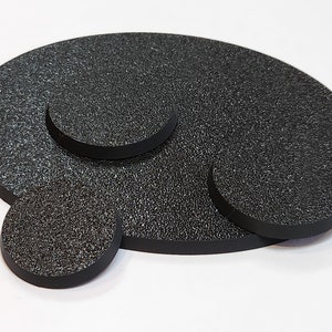 May include: Three black round bases for miniature figures. The bases are made of a textured material and have a slightly raised edge.