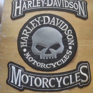 Peut inclure: Trois patchs brodés Harley-Davidson. Le patch du haut est une bannière noire avec du texte blanc qui dit "Harley-Davidson". Le patch du milieu est un cercle noir avec un crâne et des os croisés blancs et le texte "Harley-Davidson Motorcycles". Le patch du bas est une bannière noire avec du texte blanc qui dit "Motorcycles".