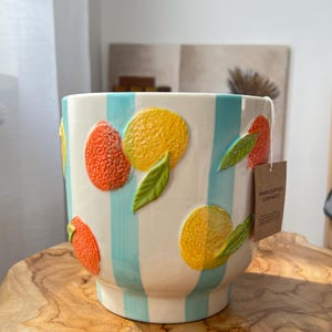 Könnte beinhalten: Ein weißer Keramiktopf mit blauen Streifen und einem Zitrusfrüchte-Design. Der Topf hat ein Etikett mit der Aufschrift "Handgefertigte Keramik".