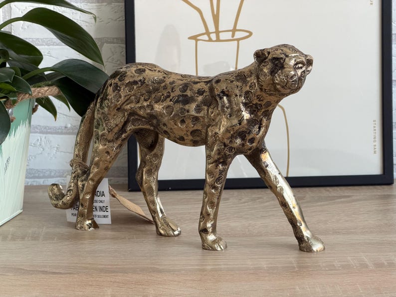 May include: A gold-coloured cheetah figurine with black spots. The sculpture is made of metal and has a textured surface. The cheetah is in a walking pose, with its head turned slightly. A decorative item.