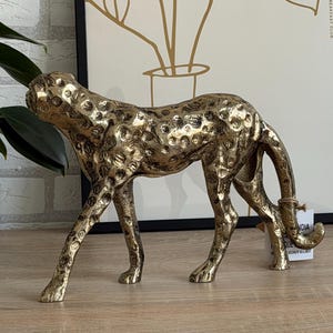 May include: A gold cheetah ornament with a textured finish and dark spots. The cheetah is depicted in a walking stance, tail curled. This decorative figurine is likely for interior design, a home decor item.