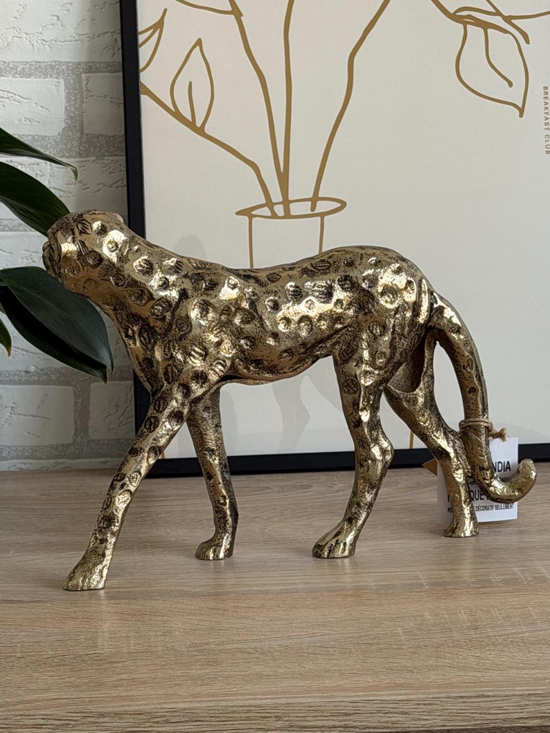 May include: A gold cheetah ornament with a textured finish and dark spots. The cheetah is depicted in a walking stance, tail curled. This decorative figurine is likely for interior design, a home decor item.
