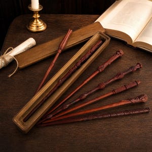 May include: A collection of six brown wooden wands with intricate carved details on the handles and shafts. One wand rests inside a long, narrow wooden box, while the others are arranged alongside it, showcasing various textures and patterns.