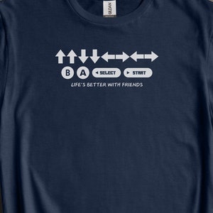 May include: A navy blue t-shirt with a white graphic of video game controller buttons and the text "LIFE'S BETTER WITH FRIENDS".