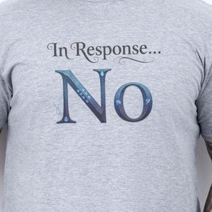 May include: A gray t-shirt with the text "In Response... No" in a decorative font. The shirt is short-sleeved and appears to be made of a soft material. The person wearing the shirt has tattoos on their arms.