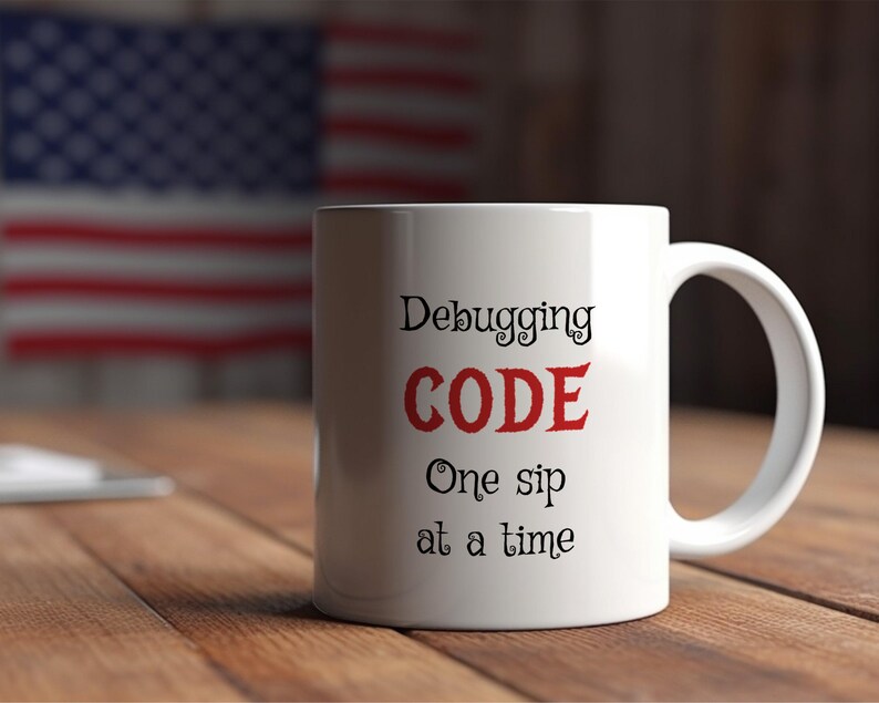 Może przedstawiać: Biały ceramiczny kubek do kawy z czarnym tekstem, kt&oacute;ry brzmi "Debugging CODE One sip at a time". Słowo "CODE" jest czerwone.
