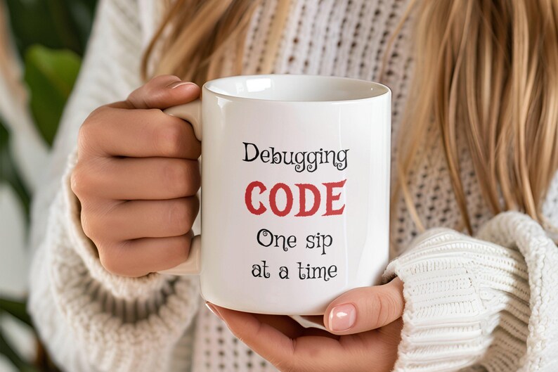 Może przedstawiać: Biały kubek ceramiczny z czarnym tekstem, kt&oacute;ry brzmi "Debugging CODE One sip at a time". Słowo "CODE" jest czerwone.
