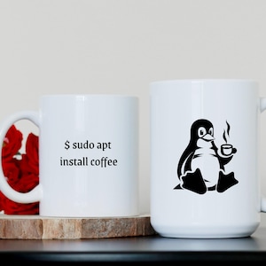 May include: White ceramic mug with a black penguin graphic holding a cup of coffee. The text "$ sudo apt install coffee" is printed on the mug.