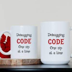 Może przedstawiać: Dwa białe kubki do kawy z czarnym tekstem i czerwonym tekstem, kt&oacute;ry brzmi "Debugging CODE One sip at a time".