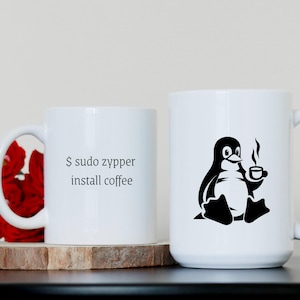 May include: Two white ceramic mugs with black designs. One mug features a penguin holding a cup of coffee with the text "$ sudo zypper install coffee". The other mug features a penguin holding a cup of coffee.