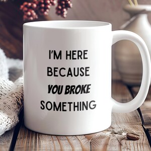 May include: White ceramic coffee mug with black text that reads "I'm here because you broke something."