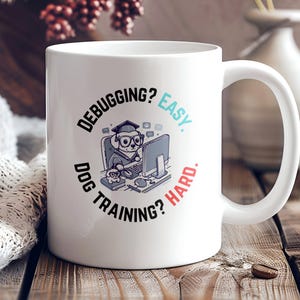 May include: White ceramic coffee mug with a black and white illustration of a dog wearing a graduation cap and sitting at a computer. The text on the mug reads "Debugging? Easy. Dog Training? Hard."