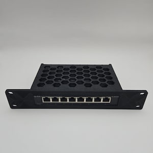 May include: Black network switch with multiple ports, featuring a honeycomb-patterned top and a front panel with the text "Tp-Link". The device has several ports for network connections.