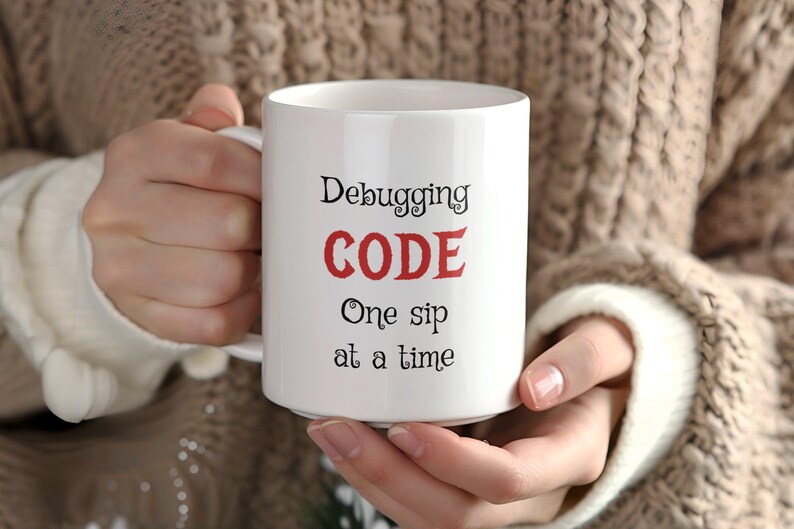 Może przedstawiać: Biały kubek ceramiczny z czarnym tekstem, kt&oacute;ry brzmi "Debugging CODE One sip at a time". Słowo "CODE" jest czerwone.