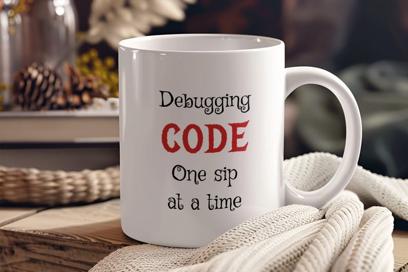 Może przedstawiać: Biały ceramiczny kubek do kawy z napisem "Debugging CODE One sip at a time" w czarnym i czerwonym kolorze.